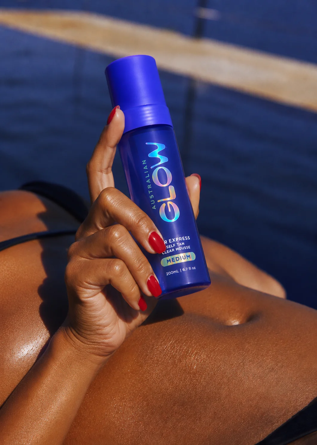 Australian Glow poolside — bronzed hand holding 1HR Express bottle