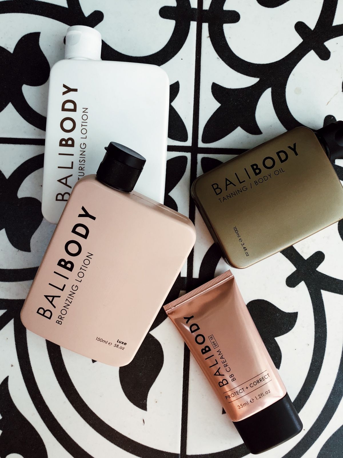 Bali Body bronzing lotion + tanning oil + BB Cream flatlay on patterned tile