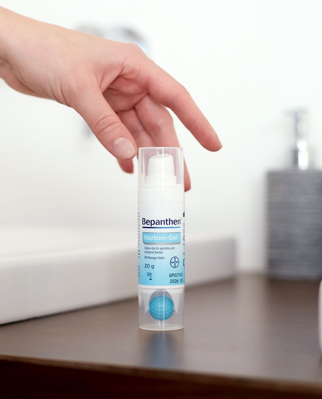 Bepanthen Narben-Gel on a bathroom counter, a hand entering the frame — domestic everyday