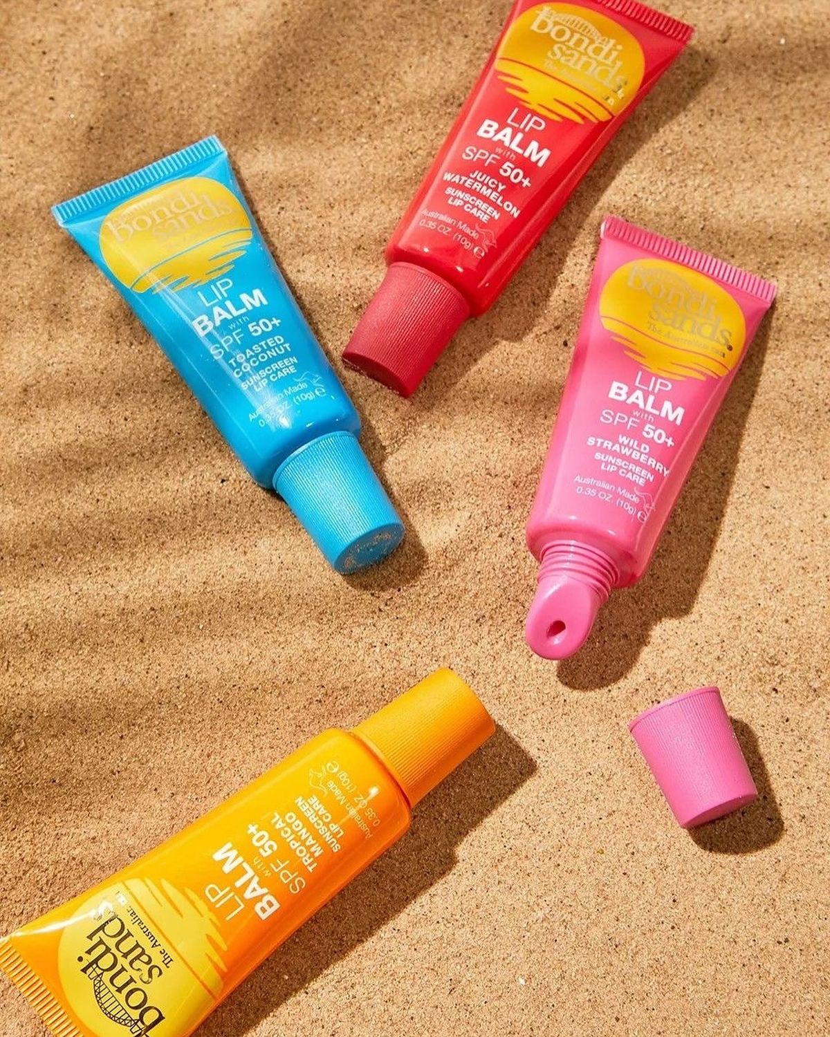 Bondi Sands lip balm range on sand — editorial flatlay