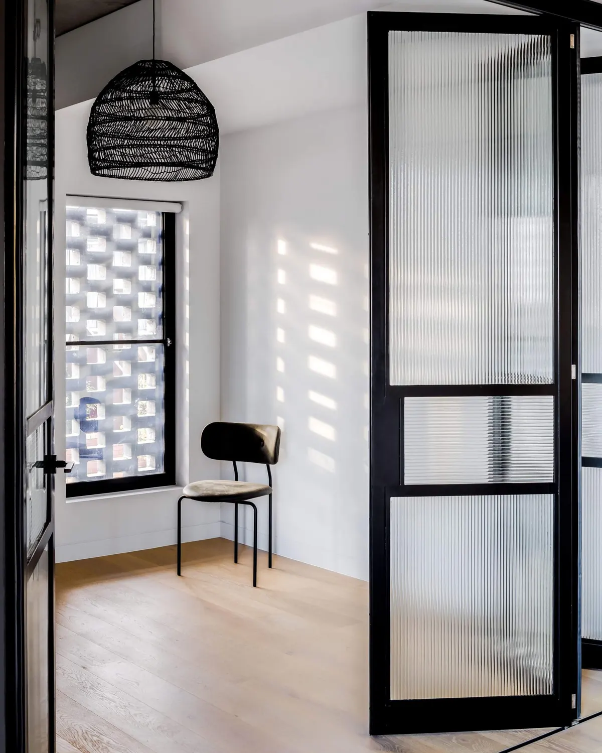 Bedroom seen through black steel-framed glass doors, under a woven pendant